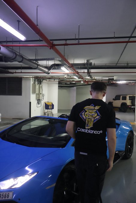 A man wearing a black "Casablanca" t-shirt stands next to a sleek blue sports car in an underground parking garage. The post "GN GN GN" likely serves as a casual sign-off or vibes caption, echoing the polished, luxe aesthetic of the scene.
