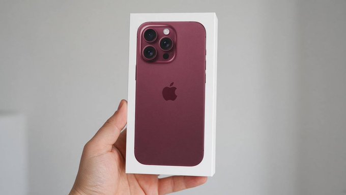 A hand holds up a sealed white iPhone box featuring a burgundy/dark red smartphone back with the Apple logo and triple-lens camera system, while the accompanying post promotes a fake "iPhone 18 Pro giveaway" with monetary prizes designed to harvest engagement through likes, comments, reposts, and follows—a common social media scam tactic.