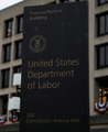 A dark blue street sign for the United States Department of Labor, with the department's seal visible, standing on what appears to be a city sidewalk with buildings in the background. The image relates to the post as the Department of Labor is the agency responsible for releasing the Consumer Price Index (CPI) data referenced in the breaking news.