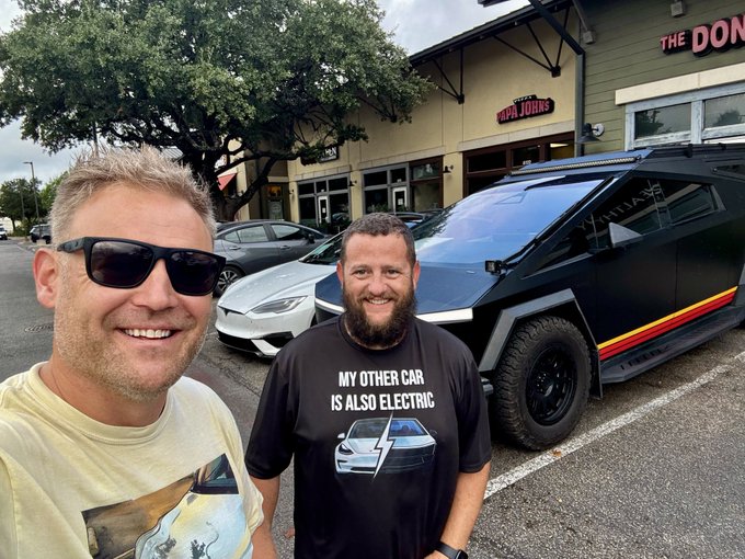 Two smiling men pose in front of a Tesla Cybertruck and a silver sedan outside a 'The Don' restaurant, with one wearing a 'MY OTHER CAR IS ALSO ELECTRIC' t-shirt featuring a Cybertruck graphic.