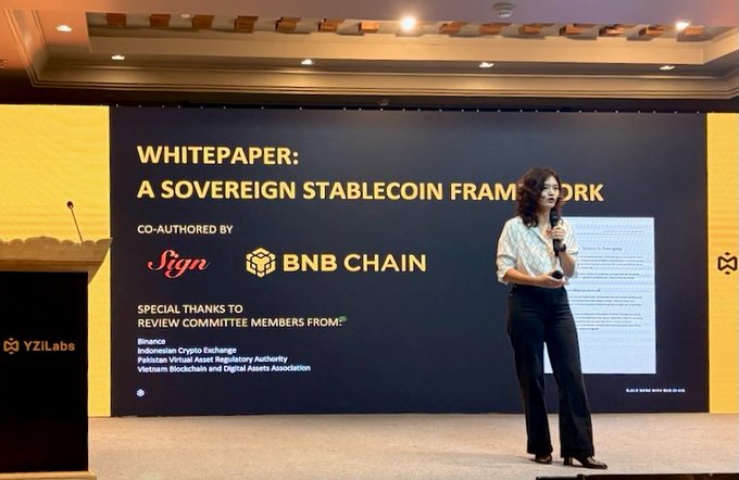 A woman in a white blouse and black trousers stands on stage presenting "A Sovereign Stablecoin Framework" whitepaper, co-authored by Sign and BNB Chain. Behind her, the screen acknowledges review committee members from Binance, Indonesian Crypto Exchange, Pakistan Virtual Asset Regulatory Authority, and Vietnam Blockchain and Digital Assets Association, illustrating the discussion on how public networks like BNB Chain enable settlement and distribution for sovereign stablecoins.