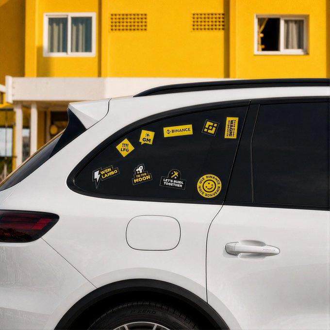 A white SUV parked in front of a yellow building displays a collection of black and yellow stickers on its rear passenger window, including ones labeled "BINANCE," "GM," "WEN LAMBO," "TO THE MOON," "LET'S BUILD TOGETHER," and "HODL BINANCE LIKE THE BTC YOU ARE." The stickers reinforce the post's playful question about the new car decals, many referencing popular crypto slang and optimism.