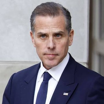 A man in a navy suit with an American flag lapel pin is shown in a close-up portrait against a light-colored stone background. The image appears to relate to the post about Hunter Biden's $LAPTOP memecoin decline, suggesting the man pictured is Hunter Biden.
