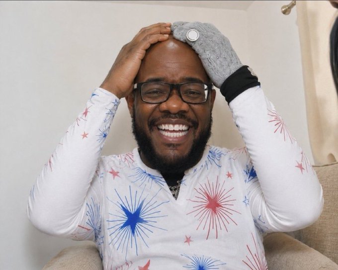 The image features a man wearing glasses, smiling at the camera while sitting down. He has a white shirt with blue stars printed on it. The background of the photo shows a wall that appears to be white, which contrasts nicely with the colorful design on his shirt. There is also an element in the image that says "X 90+5 farming tactics". This suggests that the man might have been discussing or sharing some tips related to farming techniques or agricultural practices.