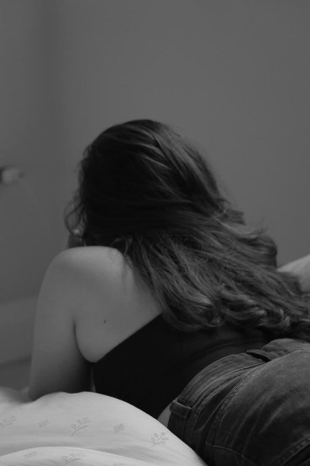 A black-and-white photo from behind captures a woman with long wavy hair wearing a black top and jeans.