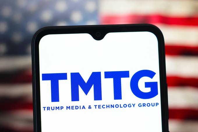 A smartphone displaying the blue 'TMTG - Trump Media & Technology Group' logo with a blurred American flag in the background.