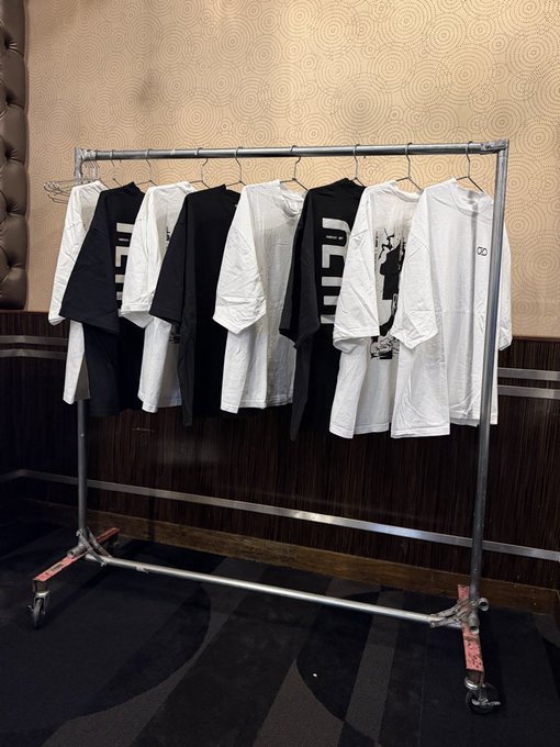 A rolling metal clothing rack displaying an assortment of black and white t-shirts hanging on hangers against a patterned wall.
