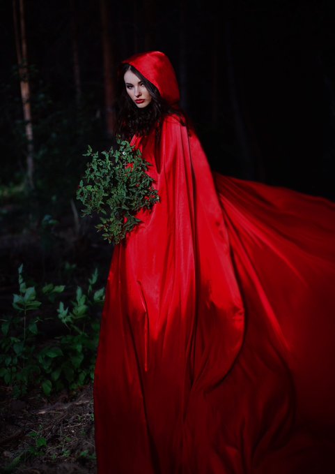 A woman in a flowing red hooded cloak stands in a dark forest holding a bouquet of greenery, styled as a fairy-tale "Red Riding Hood" photographic NFT artwork. The post promotes it as a 1/1 piece listed for 225 XTZ, shot on a Canon 5D Mark III with a 50mm lens.