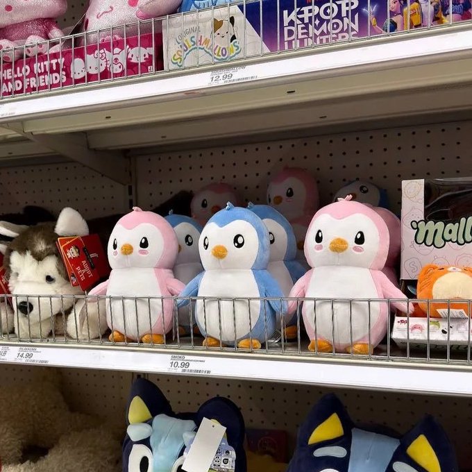 A Target store shelf displaying plush toys including pink and blue penguins, a husky, and characters from Hello Kitty, KPOP Demon Hunters, and Cocomelon, with price tags of $10.99 and $14.99.