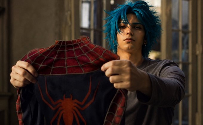 A digitally generated image of a young man with blue hair wearing a Spider-Man suit, pulling the shirt open to reveal the red spider emblem.