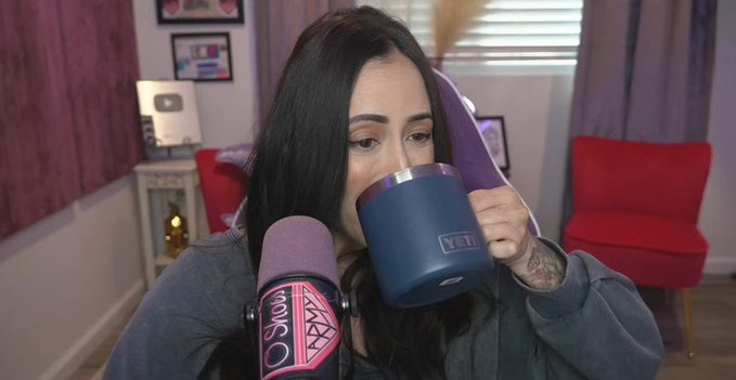 A woman with long dark hair sips from a blue YETI tumbler while sitting in front of a purple microphone branded "ASMR" in a cozy room with red chairs. The image humorously contrasts her calm, introspective moment of drinking from her mug with the post's lament about missing out on the memecoin craze.