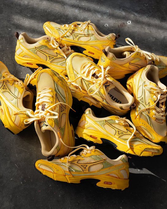 A pile of yellow, chunky athletic sneakers with mesh paneling and rope laces scattered on a dark floor.