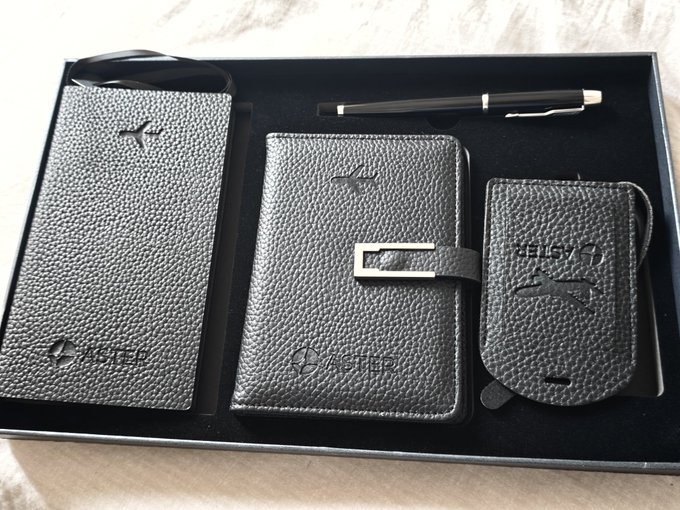 A black leather gift set from ASPER arranged in a presentation box, featuring a phone case, wallet with silver buckle, card holder embossed with a kangaroo logo, and a black ballpoint pen.