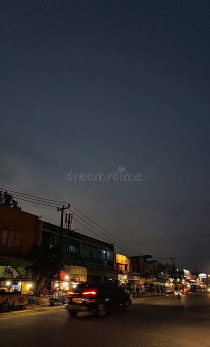 A dimly lit nighttime street scene in a small town, showing parked motorcycles, lit-up shop signs, power lines, and a dark sky, with a 'Dreamstime' watermark visible.