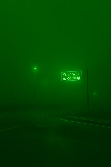 A foggy night scene with green-tinted streetlights and an illuminated neon sign reading 'Your win is coming' beside an empty road.