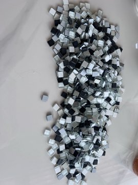 A pile of small, loose plastic building bricks in various shades of gray, black, and white scattered on a white surface.