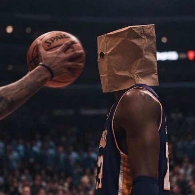 An AI-generated or heavily edited image shows a basketball player in a dark jersey with a brown paper bag over his head, standing in a stadium as another player holds a Spalding basketball nearby.
