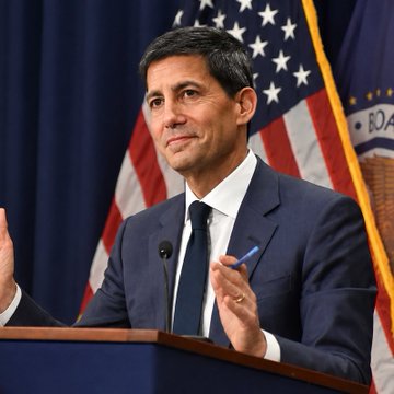 A man in a dark suit and tie stands at a podium with American flags behind him, likely a U.S. official or spokesperson addressing economic concerns. The image pairs with the post about U.S. inflation at 3.4%, suggesting a policy briefing or public address on rising prices.