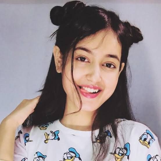 A selfie-style portrait of a smiling young woman with her hair styled in two buns, wearing a white t-shirt featuring Donald Duck prints.