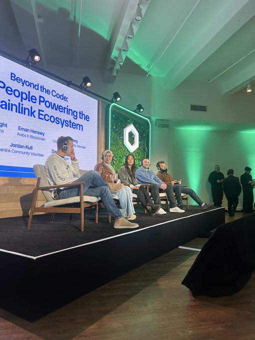 A panel discussion titled 'Beyond the Code: People Powering the Chainlink Ecosystem' featuring speakers Eman Herawy (Adobe), Jordan Kull, and others on a stage with green lighting.