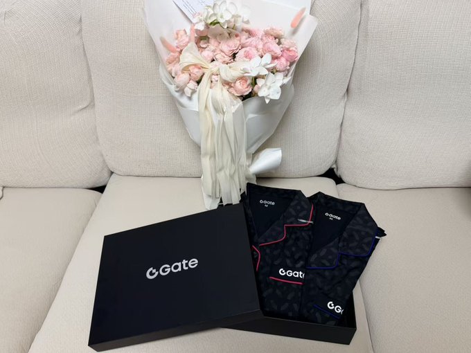 A bouquet of pink and white flowers sits on a beige couch next to a black box labeled 'Gate' containing patterned black fabric items with red and blue accents.