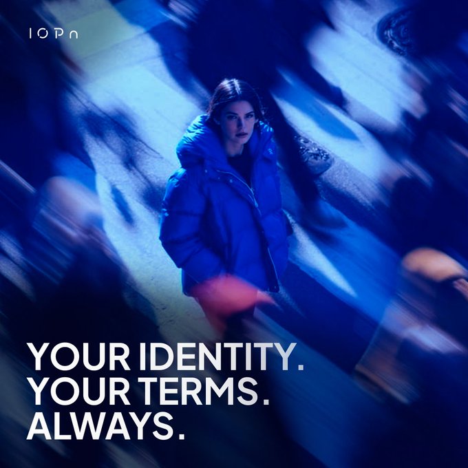 The image shows a woman wearing a blue coat standing alone, with text above her reading "Your identity. Your terms. Always." The background of the image is blurred, making it difficult to see any other people or objects. There are no texts in the image itself, but they appear to be related to the content displayed on the poster.
