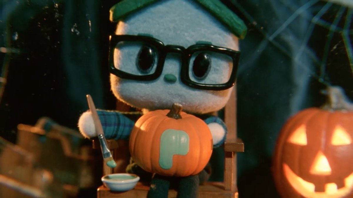A plush character wearing glasses and a beanie paints a pumpkin with a teal "P" on it, sitting beside a glowing jack-o'-lantern, playfully tying into the "Uptober" crypto celebration with the MEAD God mascot representing the project's October price-up spirit.