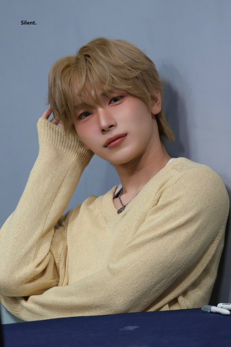 A young man with blonde hair in a cream v-neck sweater looking at the camera, with the word 'Silent.' in the top left corner.
