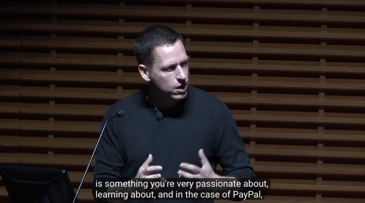 The image shows a man standing behind a podium, giving a speech or presentation. The background features a brown wall with vertical blinds covering most of the window area. There is also text visible in the image that reads "I don't believe in coincidences. I think this was all planned. I think Ripple is PayPal 2.0 I think they are finishing what they started." This suggests that the man speaking at the podium might be discussing a topic related to Ripple, PayPal or possibly both, and he could be sharing his thoughts on the subject matter with an audience.