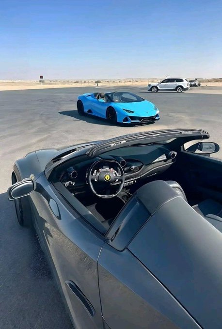 A first-person view from a gray convertible luxury car, with a blue sports car parked ahead and a white SUV in the distance on a desert road, paired with a caption discussing a "happy new week" and promoting the @FIH_USD1 ecosystem by connecting prediction markets with USD1-powered DeFi. The image of high-end vehicles symbolizes the prosperity and success associated with the crypto project's utility and liquidity goals.