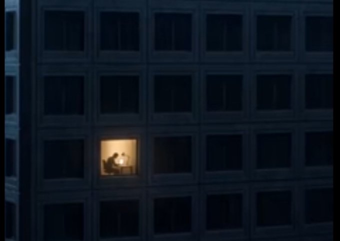 A dimly lit office building at night shows a single illuminated window where a silhouetted figure works at a desk with a lamp, while all surrounding windows remain dark. The image powerfully illustrates the post's message about dedication and effort—while others rest, the individual toiling alone represents the discipline required to build generational wealth.