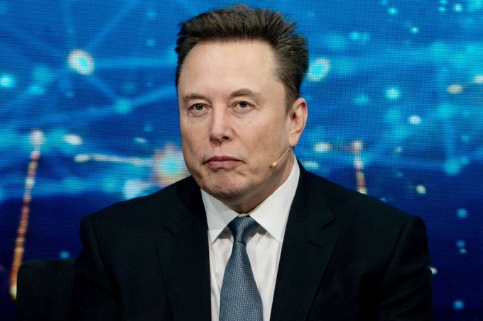 The image features a man dressed in formal business attire with a tie, seated at a desk facing forward. He appears to be looking off into the distance or pondering over something. The background consists of a blue-green color scheme, which contrasts with the man's dark clothing and adds depth to the scene. The post appears to discuss the relationship between Bitcoin adoption and the space exploration company, SpaceX, indicating that this might be an article discussing financial or technological trends involving these two entities.