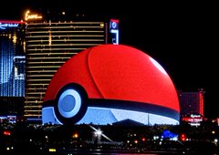 A massive Poké Ball sphere displayed on a building at night, resembling Las Vegas casino architecture with city lights below.