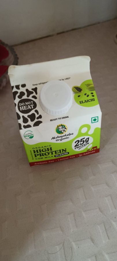 A small carton of 'Akshayakalpa Organic High Protein Cow Milk Elaichi' flavored milk, labeled 25g protein, antibiotic-free, and ready to drink.