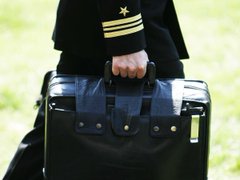 The image shows a hand gripping a military-style black duffel bag, worn by someone in a dark uniform adorned with gold sleeve insignia and a star emblem. The bag and uniform evoke themes of discipline and readiness, symbolically tying into $ClawBank's message about understanding its deeper meaning and purpose.