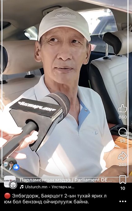 The image shows a man being interviewed with a microphone bearing the text "Мастерч.мн". The accompanying post questions if the "Binance scandal" is related to "Elbegdorj" and expresses concern about the younger generation's critical thinking, implying the man in the image may be involved in discussions or news related to these topics.