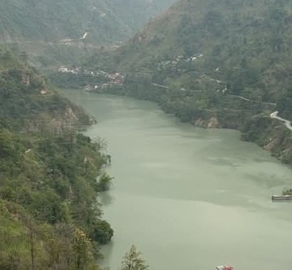 An aerial landscape view of a green river winding through forested mountains, with a small village visible in the distance.