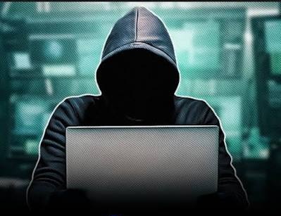A hooded figure in a dark sweatshirt sits behind a laptop with a blank white screen, set against a glitchy green background.
