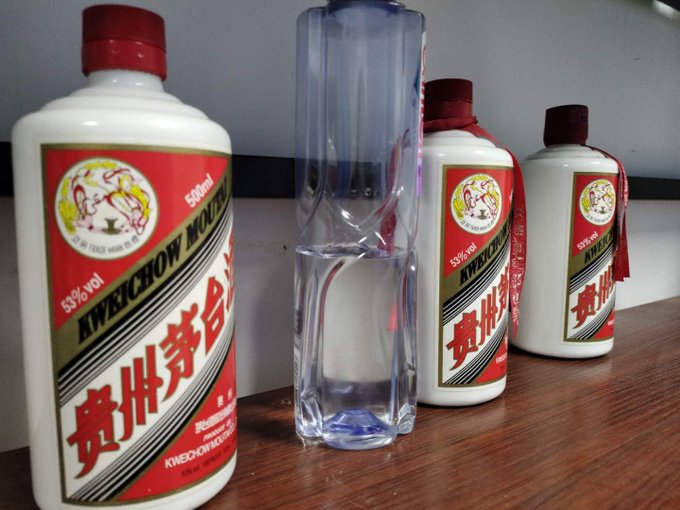 Three bottles of Kweichow Moutai (53% vol, 500ml) baijiu liquor with distinctive red, white, and gold labels, displayed alongside a clear glass on a wooden surface.