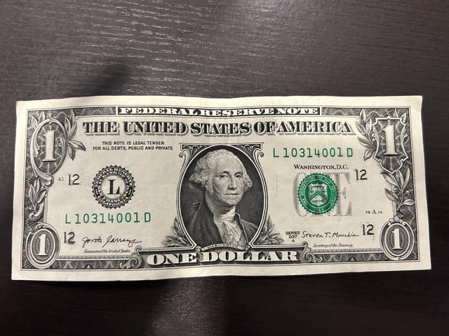 A United States one dollar bill (Federal Reserve Note, Series 2017) lying on a dark wooden surface.