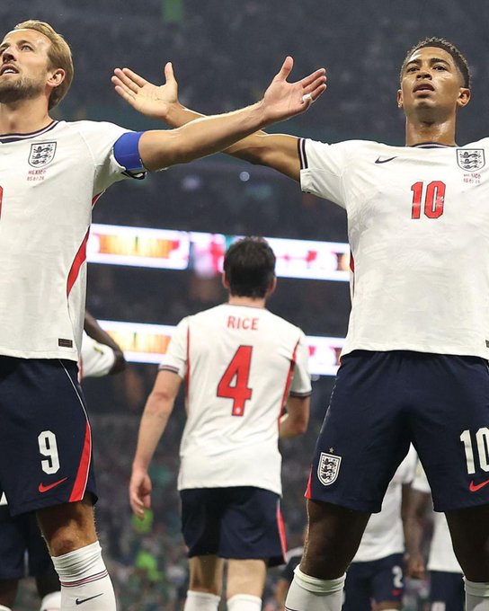 England soccer players Harry Kane (#9, wearing the captain's armband) and Jude Bellingham (#10) stand with arms outstretched in celebration, while Declan Rice (#4) is visible in the background.