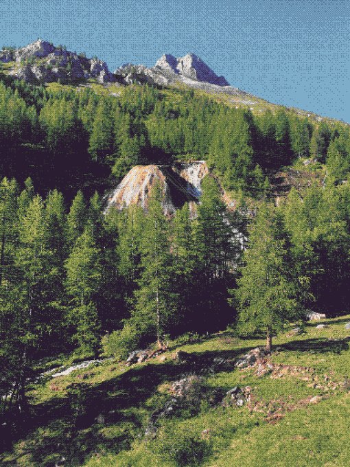 A scenic mountain landscape features rocky peaks, dense green coniferous forest, and a grassy meadow in the foreground under a clear blue sky.