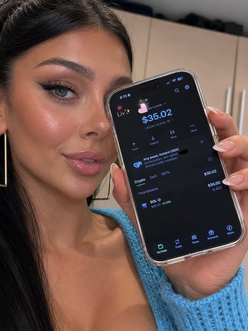 The woman in the image is holding up her smartphone, displaying the amount of money she has set aside each week for trading options. She is wearing a blue sweater, which matches the color scheme of her phone case, creating a visually pleasing scene. The post encourages her to put $35 into $SOL every week until the end of the week on ATH week 1, suggesting a disciplined approach towards investing in options.