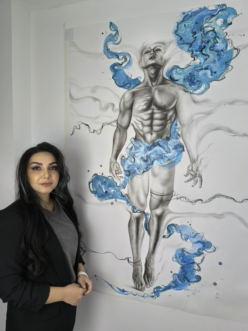 A woman with long dark hair in a black blazer stands next to a large artwork depicting a gray, anatomical male figure surrounded by swirling blue and white smoke or water.