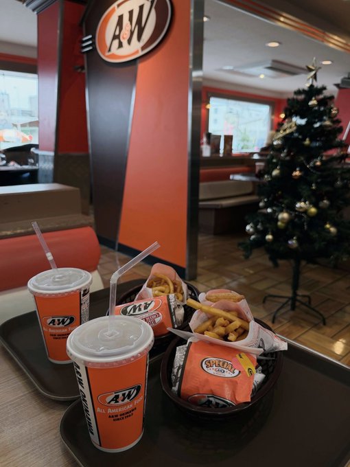 Two trays of food and drinks at an A&W restaurant, with a decorated Christmas tree visible in the background.