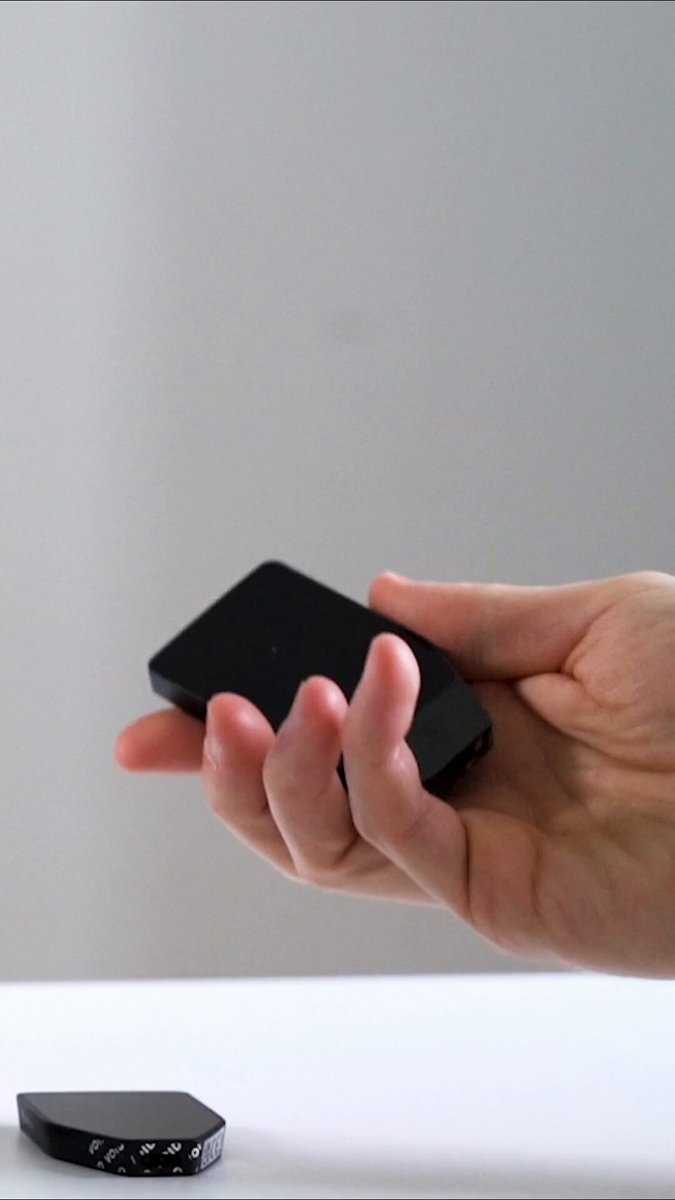 The image shows a person holding a black electronic device, possibly a smartphone or tablet, over a white surface. The device appears to be a small square-shaped object with a screen that can be held in one hand. In the background, there is another smaller square-shaped object placed on the same white surface. The image also contains text that reads "A chip vulnerability was found in the @Trezor Safe by the @Ledger security team". This suggests that someone has discovered a vulnerability in the @Trezor Safe and notified both companies about it, which could potentially lead to security issues or privacy concerns for users of the device.