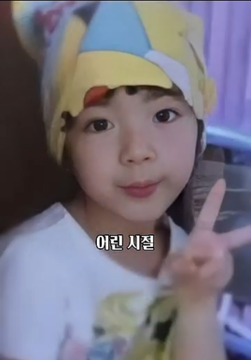 A young child wearing a yellow and blue character hat, smiling and making a peace sign, with the Korean text '어른 시절' overlaid on the image.