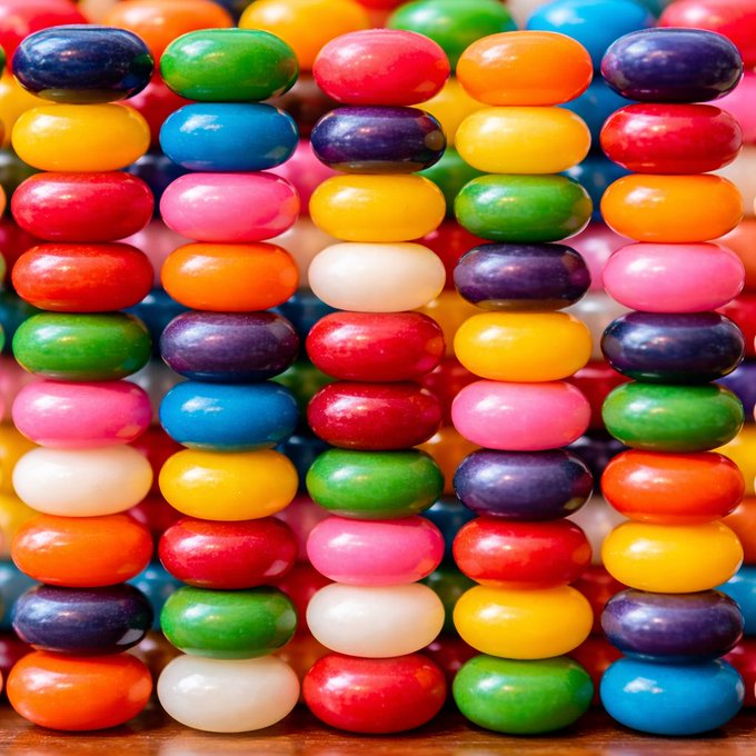 A close-up image of stacked colorful candy discs arranged in rows, featuring various colors including red, blue, green, yellow, orange, pink, white, and purple.