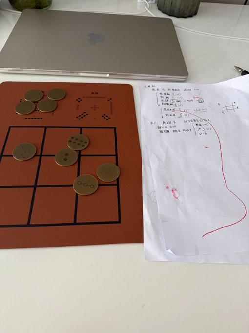 The image shows two objects placed on a white table - an open laptop computer and a game board with coins scattered across its surface. The laptop screen displays a post about Bitcoin, specifically mentioning the Summer Solstice and the Jia Wu month. This suggests that someone might be using their time to play a coin-based board game or possibly researching the history of Bitcoin during this particular season.