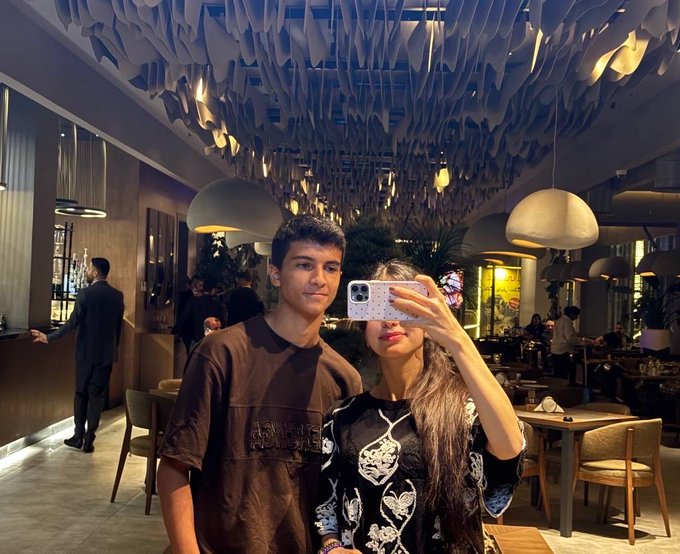 A young man and woman take a selfie together inside a restaurant with distinctive hanging paper decorations from the ceiling.